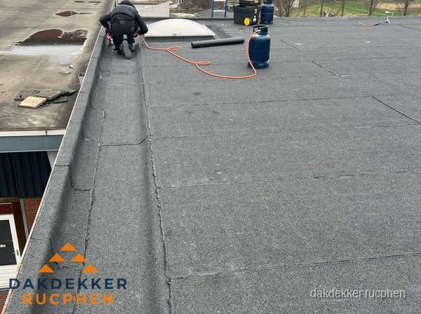 Dakdekker repareert bitumen dakbedekking op groot plat dak in Rucphen